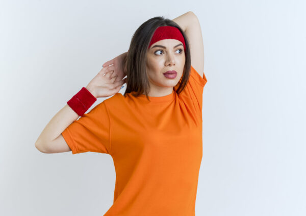 Young sporty woman wearing headband and wristbands keeping hands together behind head looking at side exercising isolated on white background with copy space